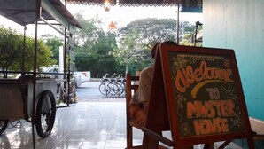 A signboard with "Welcome to MISTER HOUSE" written on it, placed in a covered outdoor area with bicycles and a parked car in the background. - Muster House - Hostel (Ayutthaya)