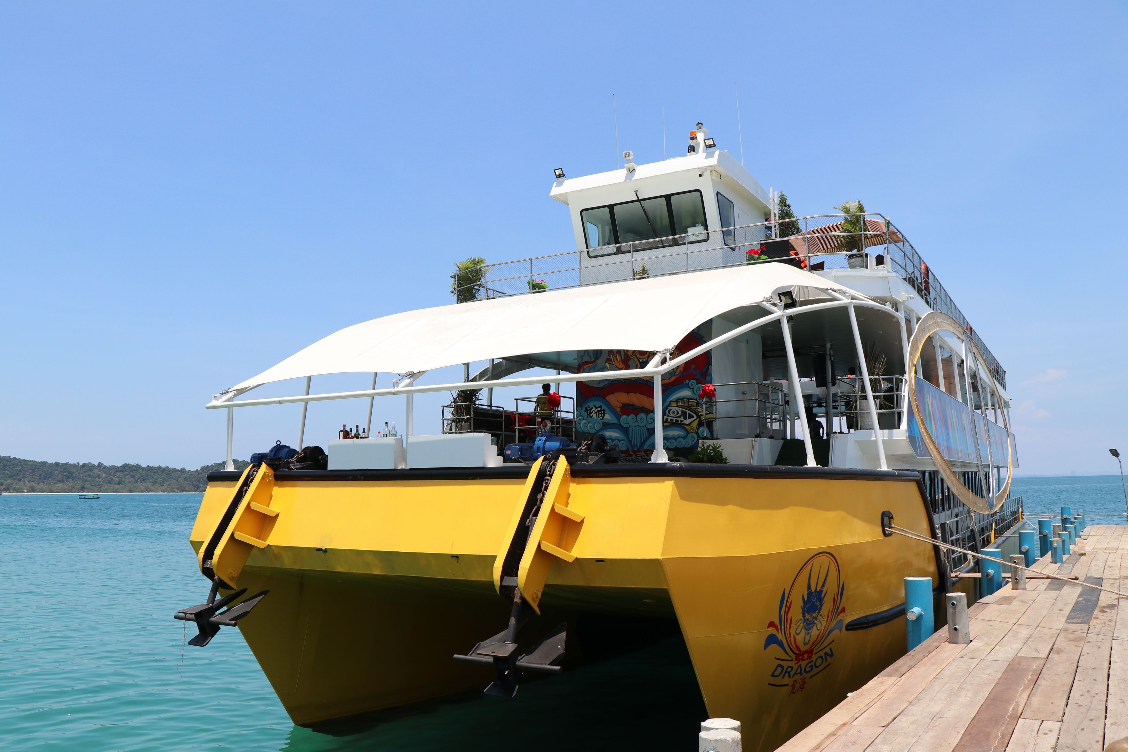 A yellow boat docked at a pier with a clear blue sky and calm sea in the background.
