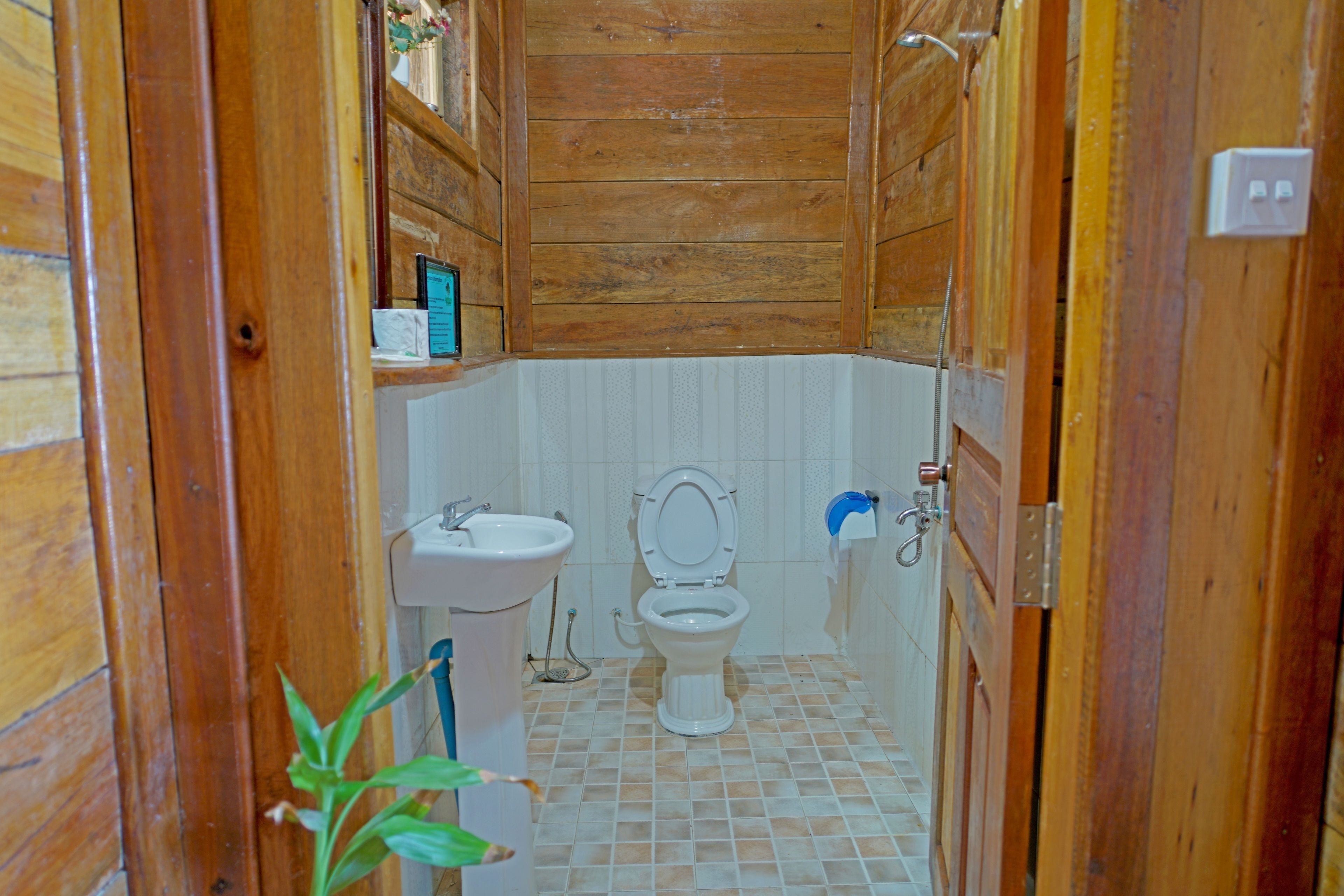 A wooden-paneled bathroom with a toilet, sink, and shower.
