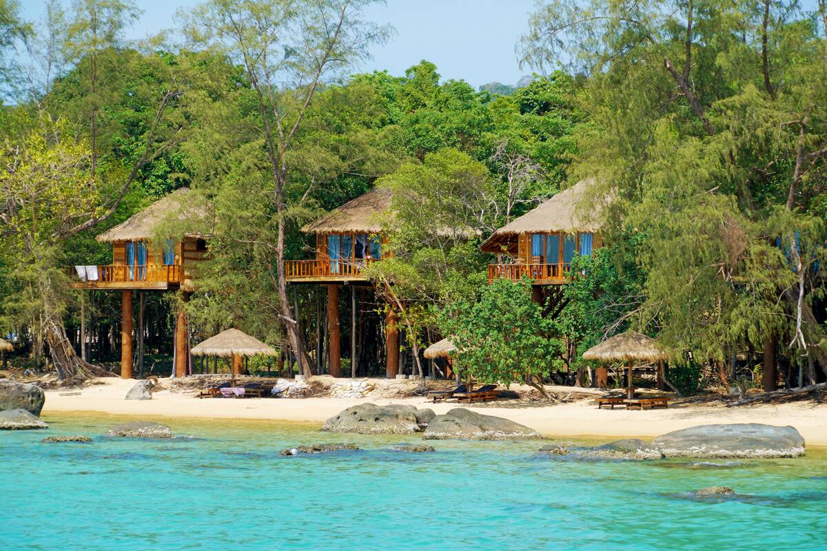 A beachfront property with thatched-roof cabins, a sandy beach, and a clear view of the ocean.