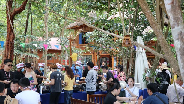 An outdoor dining area with wooden tables and benches, surrounded by trees and a building with a thatched roof. - Tree House Bungalows Resort (Koh Rong)