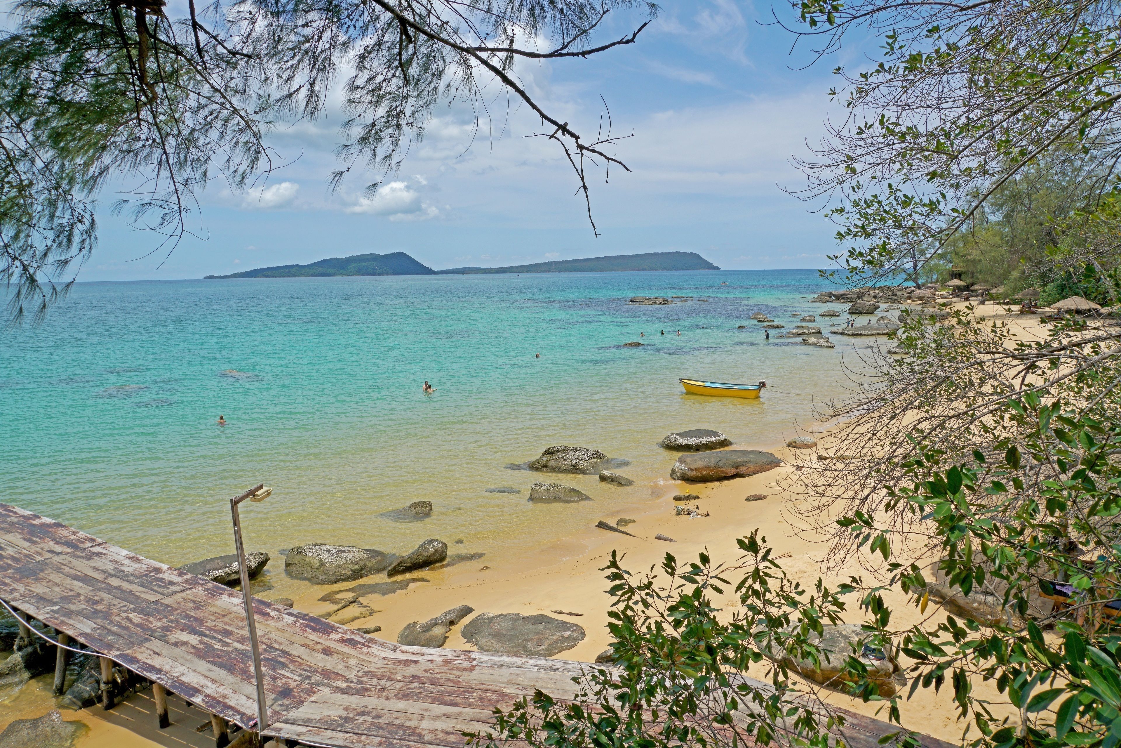 Ein Strand mit klarem türkisblauem Wasser, felsigem Ufer und einer Holzkonstruktion.