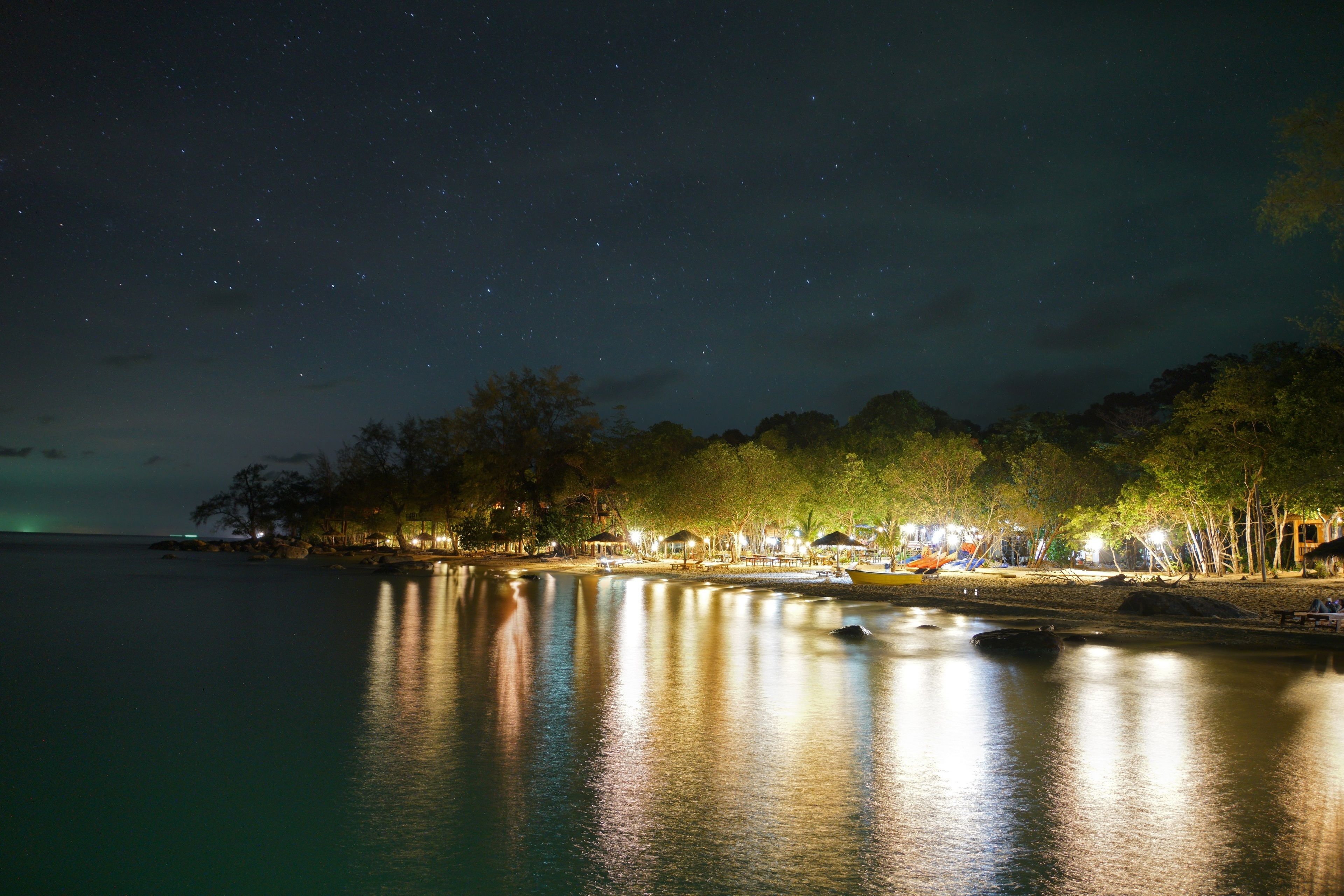 Une scène de plage nocturne, avec des eaux calmes reflétant les lumières provenant du rivage.