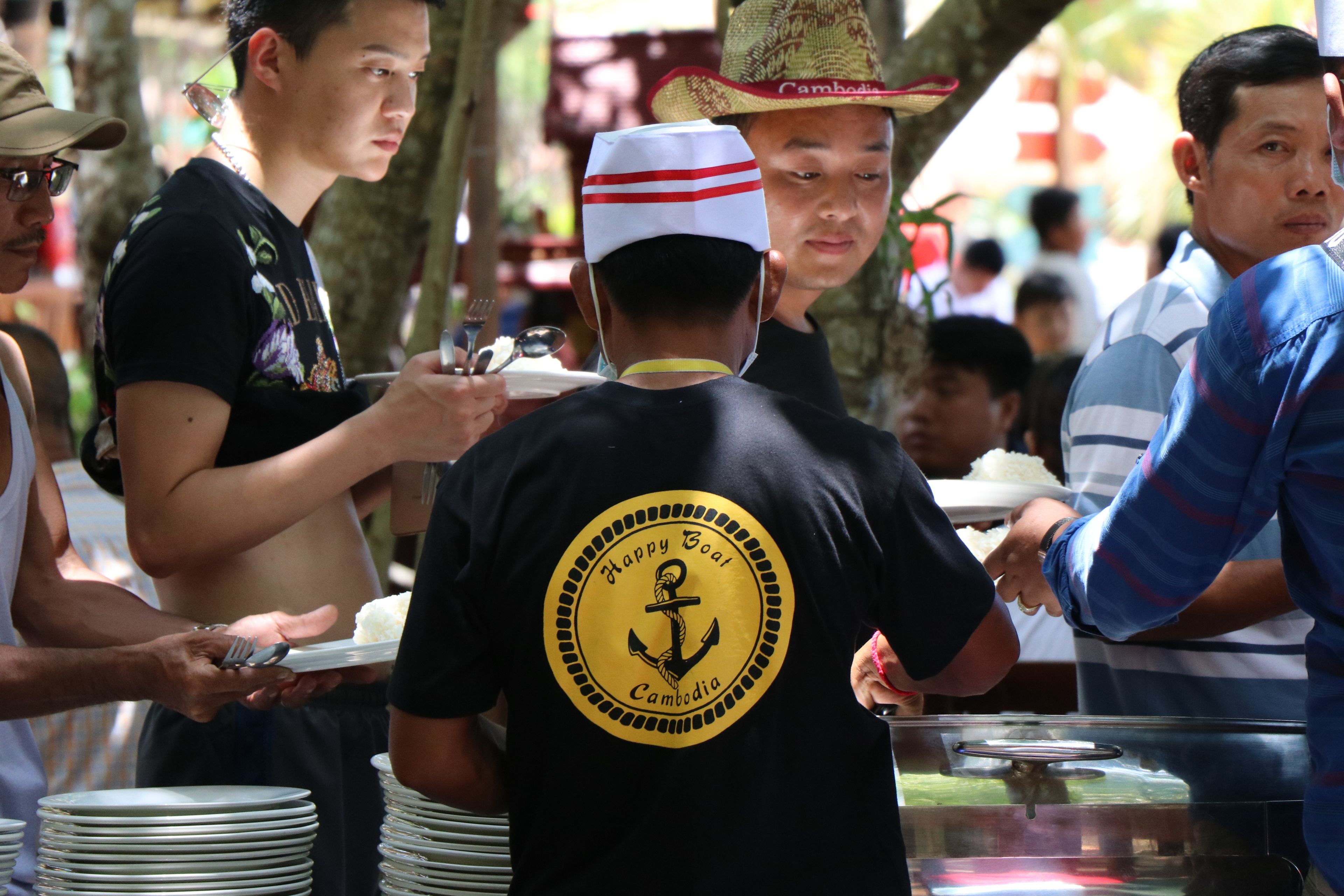 A group of people at a food stall with a sign that reads "Happy Boat Cambodia".
