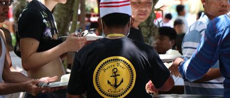 A group of people at a food stall with a sign that reads "Happy Boat Cambodia".