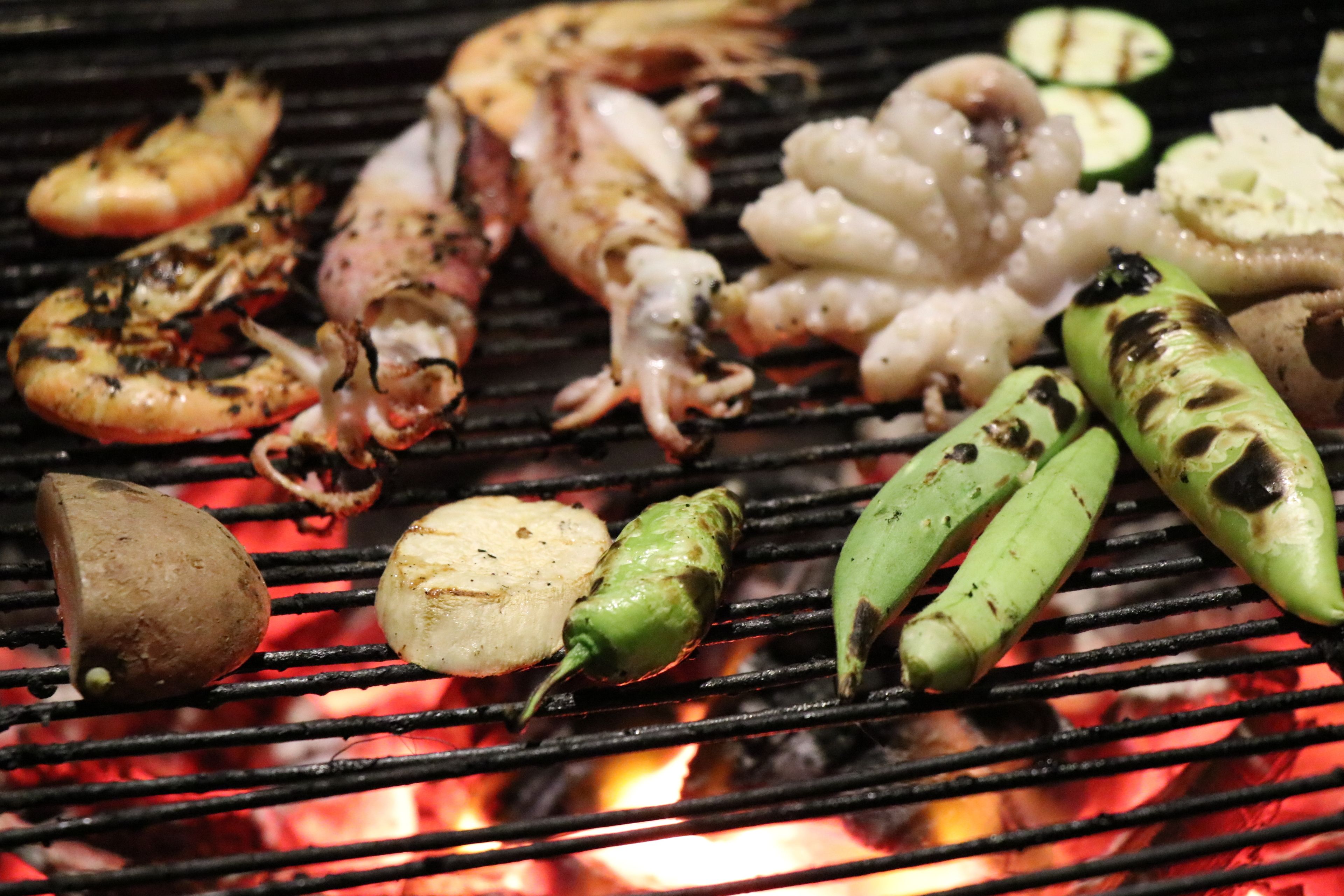 Grilled shrimp, squid, and vegetables on a grill over an open flame.