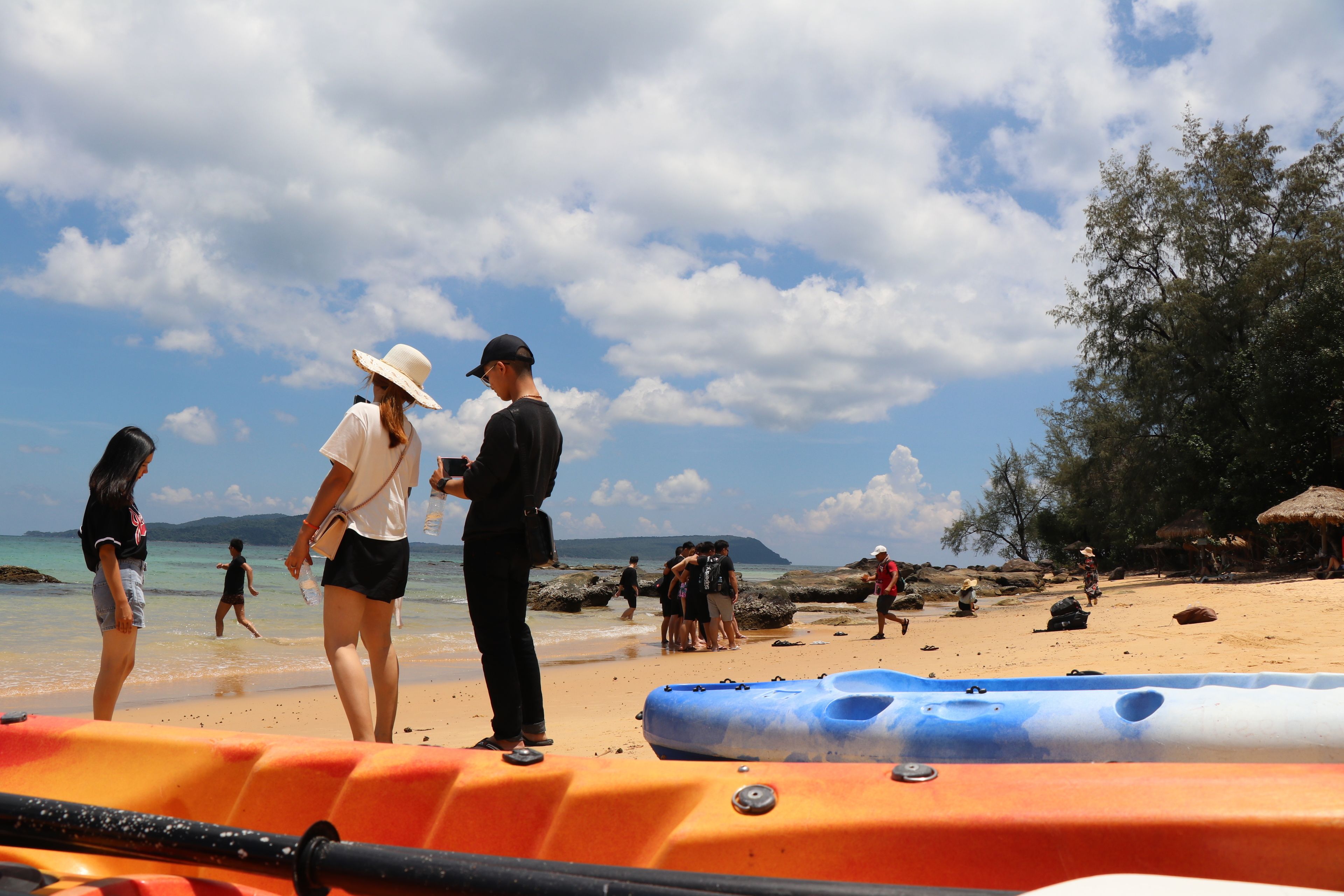 A beach scene with people, a blue inflatable raft, and a thatched-roof hut.