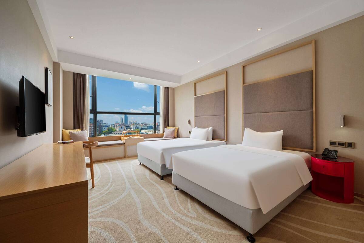 Habitación de hotel con dos camas, un escritorio, un televisor y vistas a la ciudad.