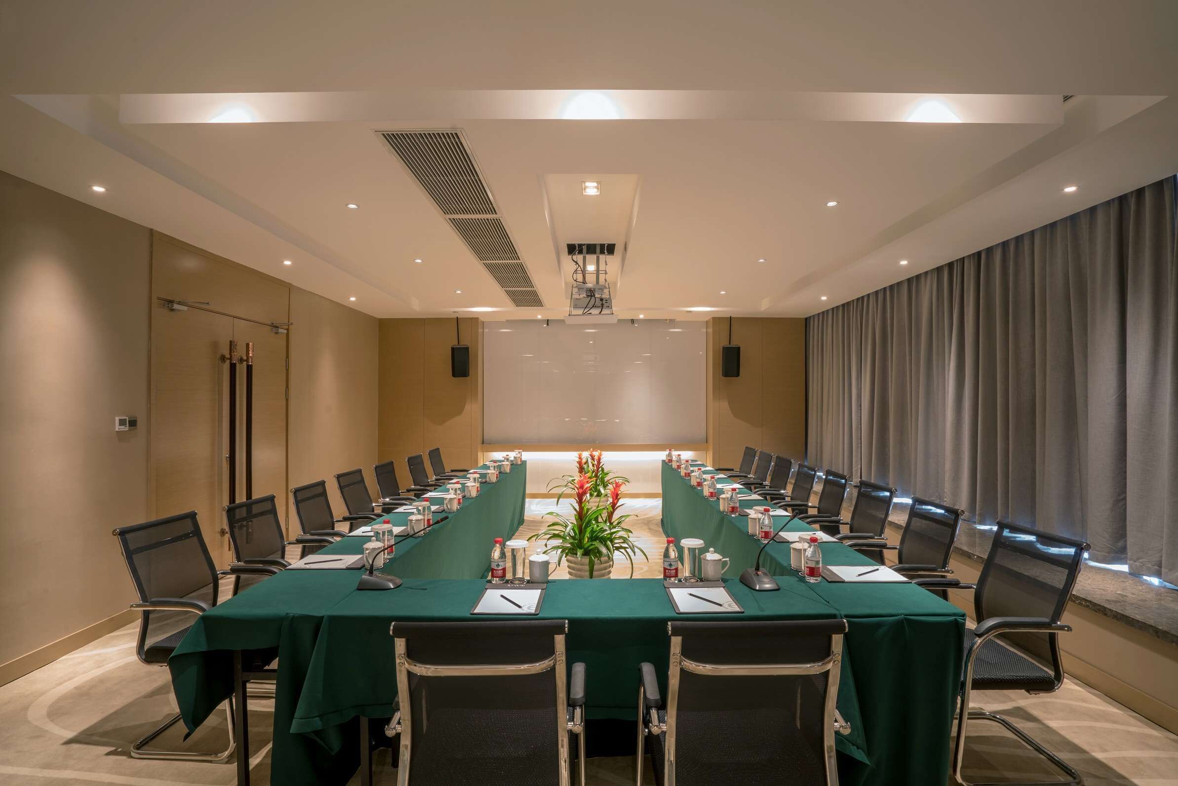 A conference room with a long table, chairs, and a projector screen.