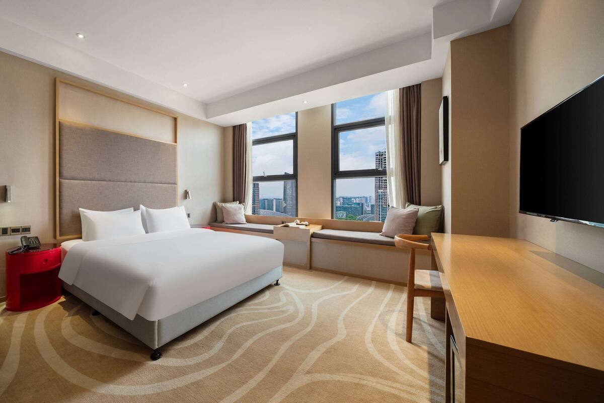 Habitación de hotel con una cama grande, un escritorio, un televisor y una ventana con vistas a la ciudad.