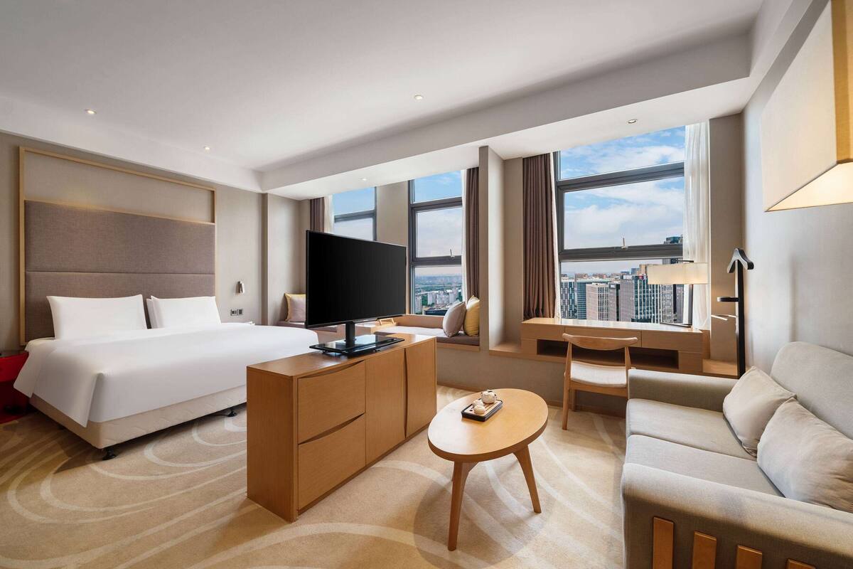Una habitación de hotel moderna con una cama grande, un escritorio, un sofá y un televisor.