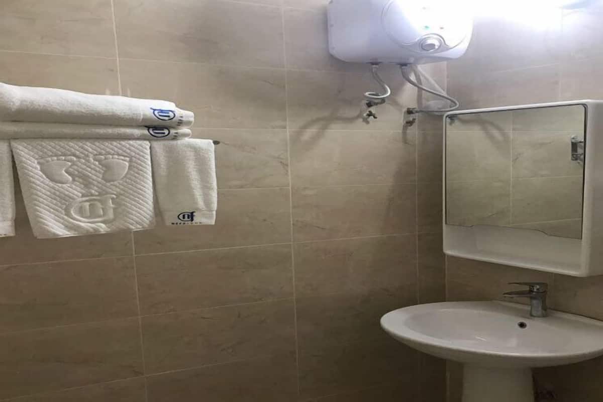 Een badkamer met behang van beige tegels, een witte wastafel en een spiegel erboven. Twee handdoeken hangen aan de muur.