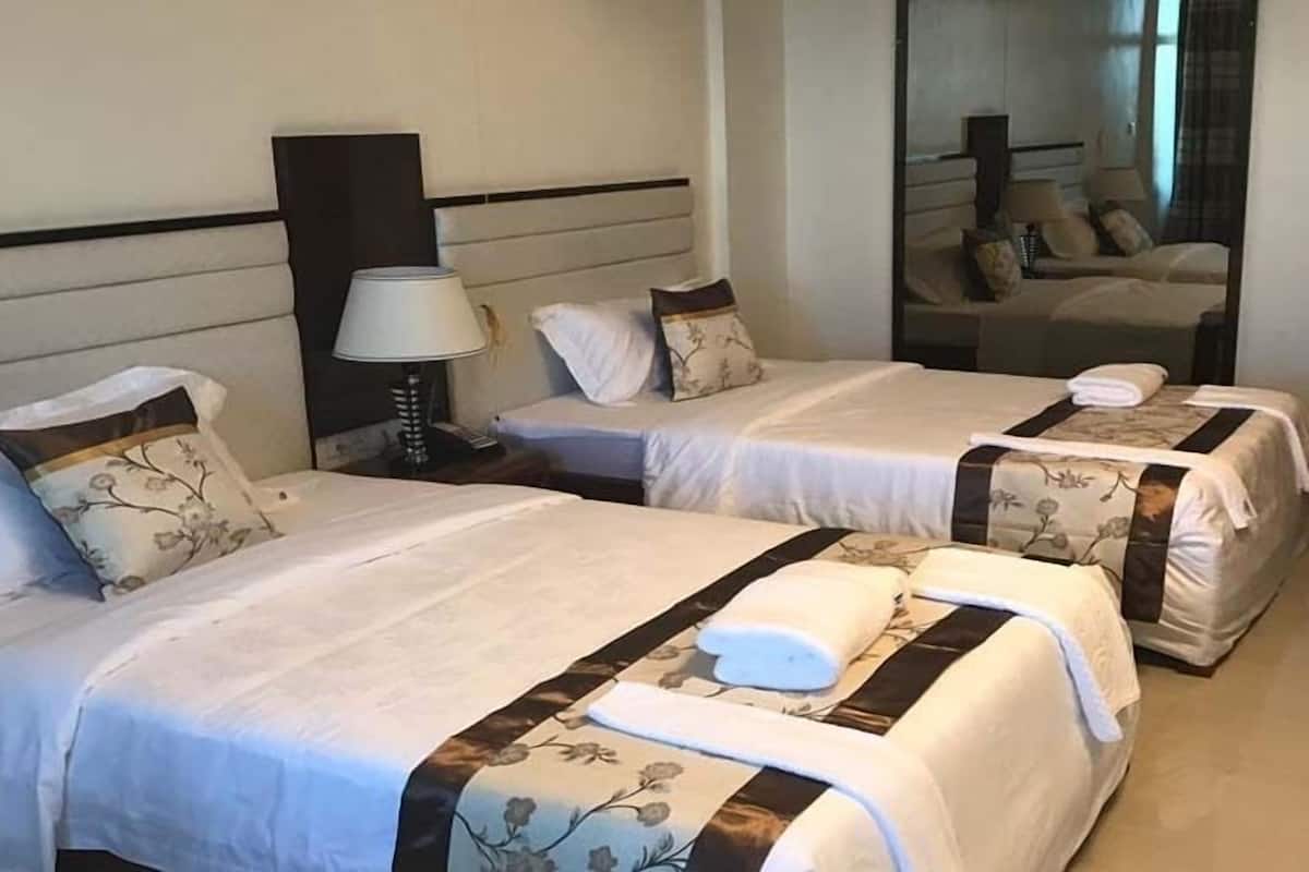Een hotelkamer met twee bedden, elk met een bloemenprint deken en bijpassende kussens. Daartussen staat een nachtkastje met een lamp, en aan de muur hangt een spiegel.