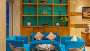 A lobby with blue sofas, wooden chairs, a small round table, and a teal-colored shelving unit with decorative items. - Hotel Amritsar International (Amritsar)