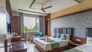 A hotel room with a large bed, a desk, a chair, and a view of the city. - Hotel Amritsar International (Amritsar)