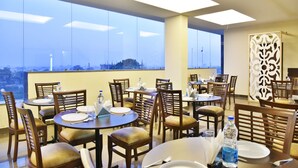 A dining area with round tables and chairs, large windows, and a decorative wall panel. - Hotel Amritsar International (Amritsar)