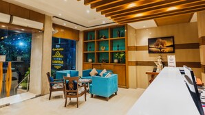 A hotel reception area with a long reception desk, blue sofas, wooden paneling, and a large window with a view of greenery. - Hotel Amritsar International (Amritsar)