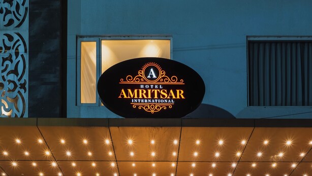 The exterior of the Amritsar International Hotel with a well-lit entrance, steps leading up to the door, and potted plants around the entrance area. - Hotel Amritsar International (Amritsar)
