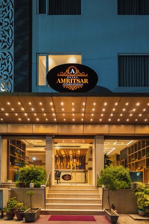 The exterior of the Amritsar International Hotel with a well-lit entrance, steps leading up to the door, and potted plants around the entrance area. - Hotel Amritsar International (Amritsar)