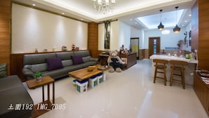 A modern living room with a sofa, coffee table, and a teddy bear. There is a kitchen area with a bar and stools. - Tu Wei 192 (Zhuangwei)