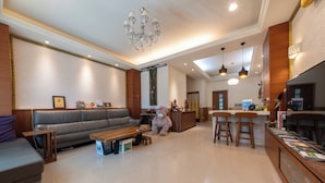 A spacious living area with a sofa, a coffee table, and a large teddy bear. There is a kitchen area with bar stools and a counter. - Tu Wei 192 (Zhuangwei)