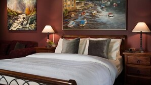 A neatly made bed with a wooden headboard, two bedside tables with lamps, and a painting of boats on a river on the wall. - Impressions Studio (Daylesford)