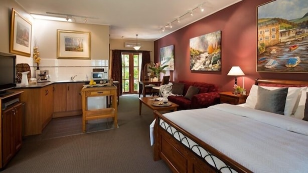 A hotel room with a bed, a desk, a chair, a TV, and artwork on the walls. - Impressions Studio (Daylesford)