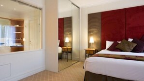 A hotel room with a large bed, a wardrobe, a mirror, and a small table with a lamp. - Lakeside Suites 2 (Daylesford)