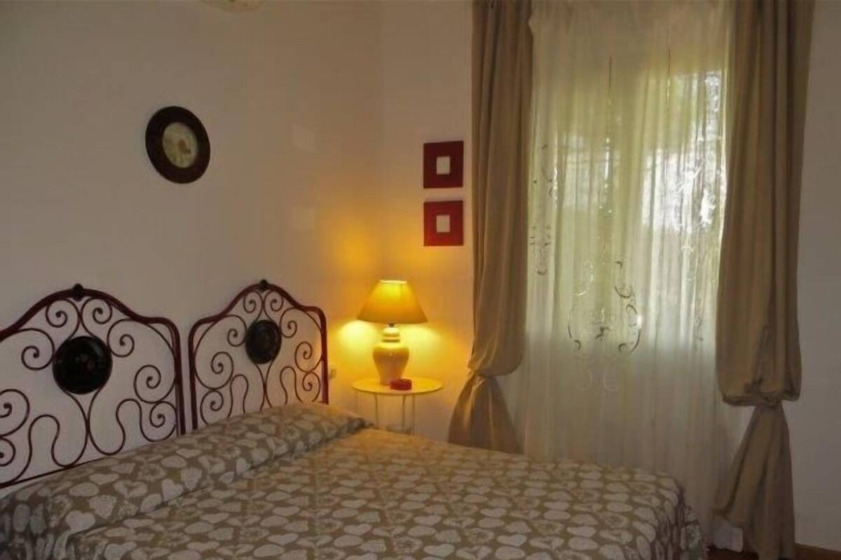 A bedroom with a bed, a bedside lamp, a wall clock, and a window with curtains.