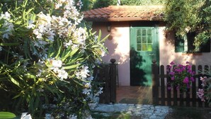 Una casa rústica con una puerta verde, rodeada de abundante vegetación y plantas en flor.