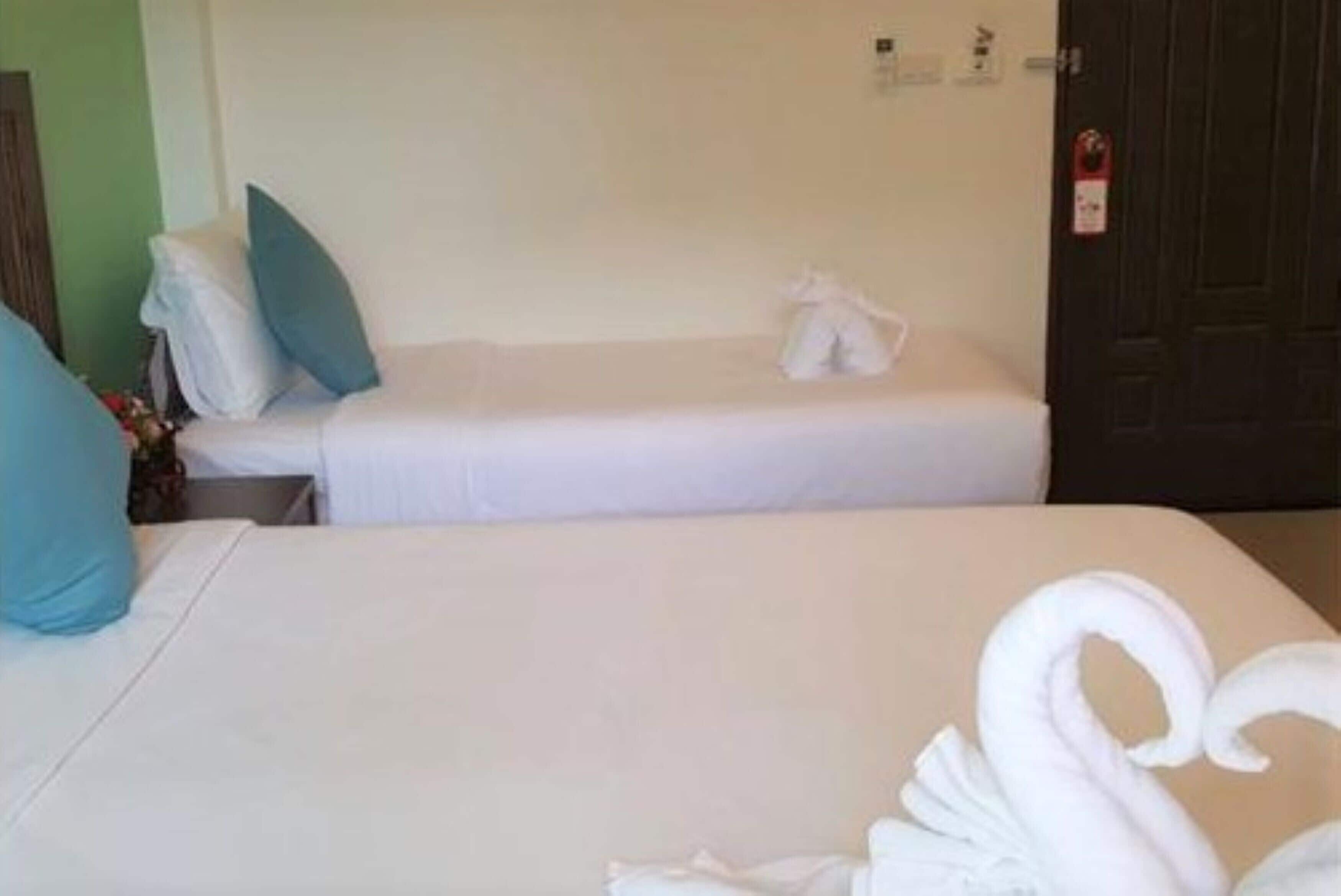 Une chambre d’hôtel avec deux lits, chacun étant agrémenté de draps blancs et d’un seul oreiller bleu. Un drapé blanc est posé sur l’un des lits et un cygne décoratif sur l’autre.