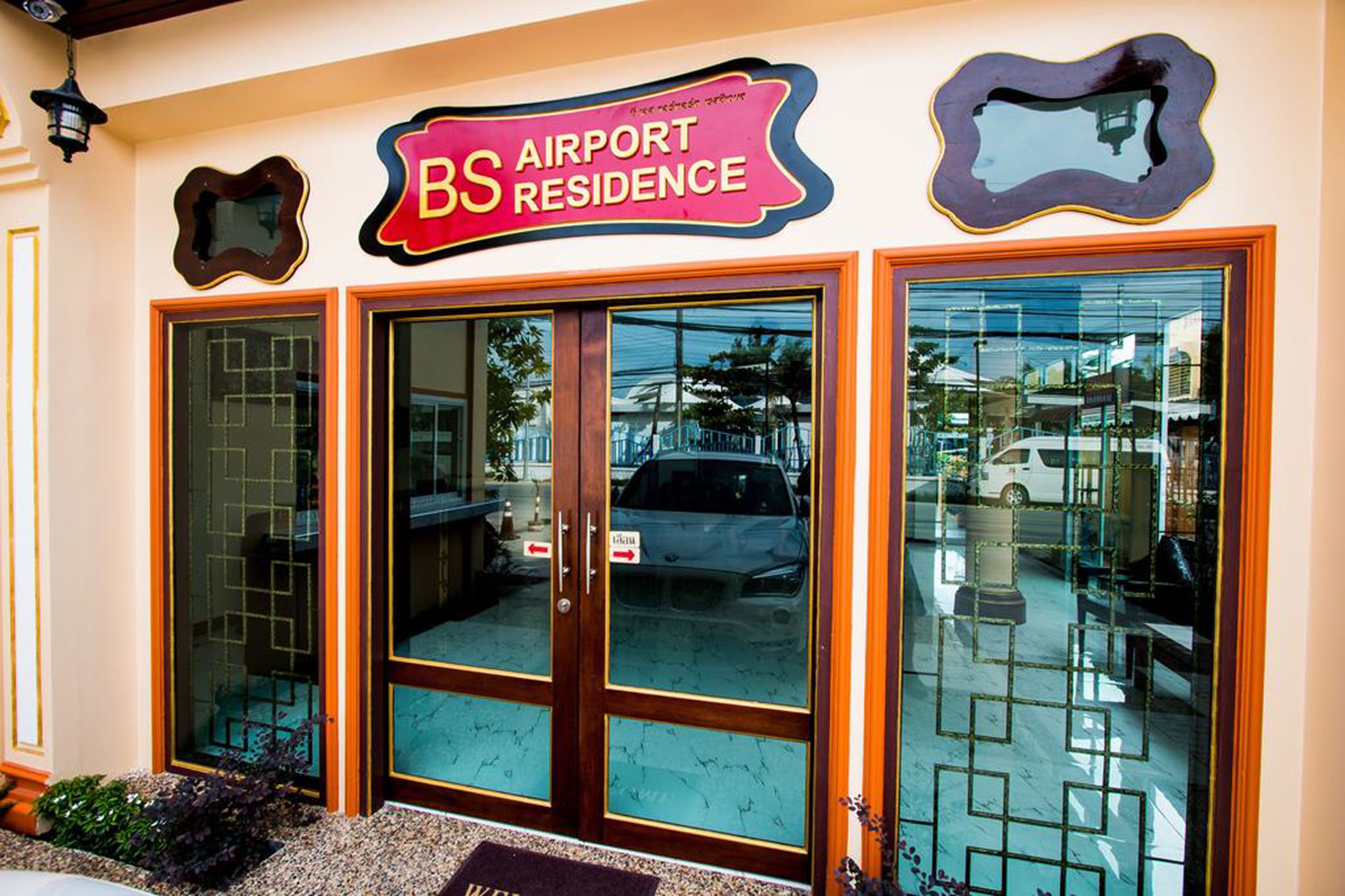 Entrada de un hotel con un letrero que dice "BS AIRPORT RESIDENCE", amplias puertas de vidrio y el reflejo del exterior.