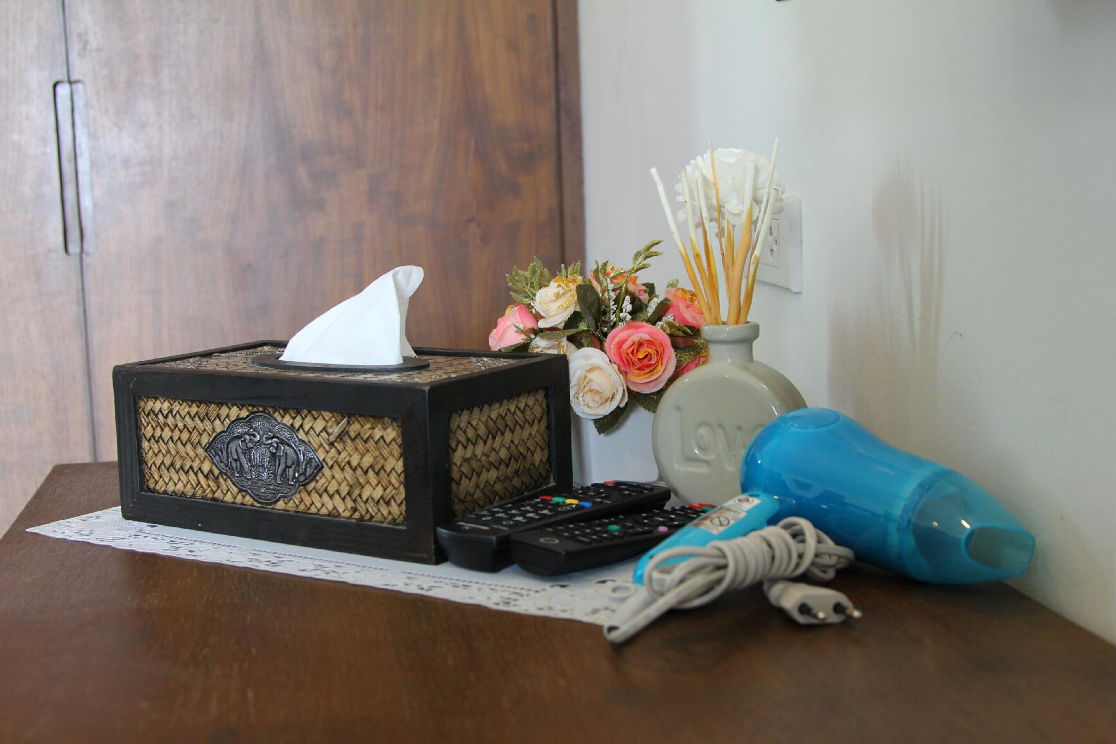 A wooden table with a tissue box, remote controls, a vase with flowers, and a blue water bottle.