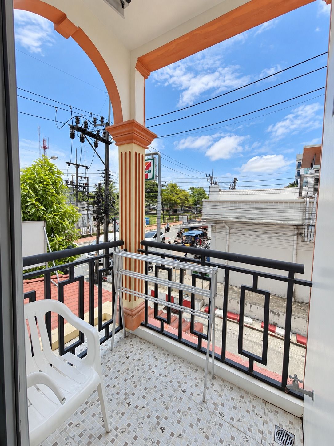Un balcone con vista su una strada, un negozio di alimentari 7-Eleven e un pavimento piastrellato.