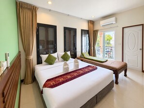 A hotel room with a large bed, a bench with cushions, a view of the outside, and a door. - BS Airport at Phuket (Sa Khu)