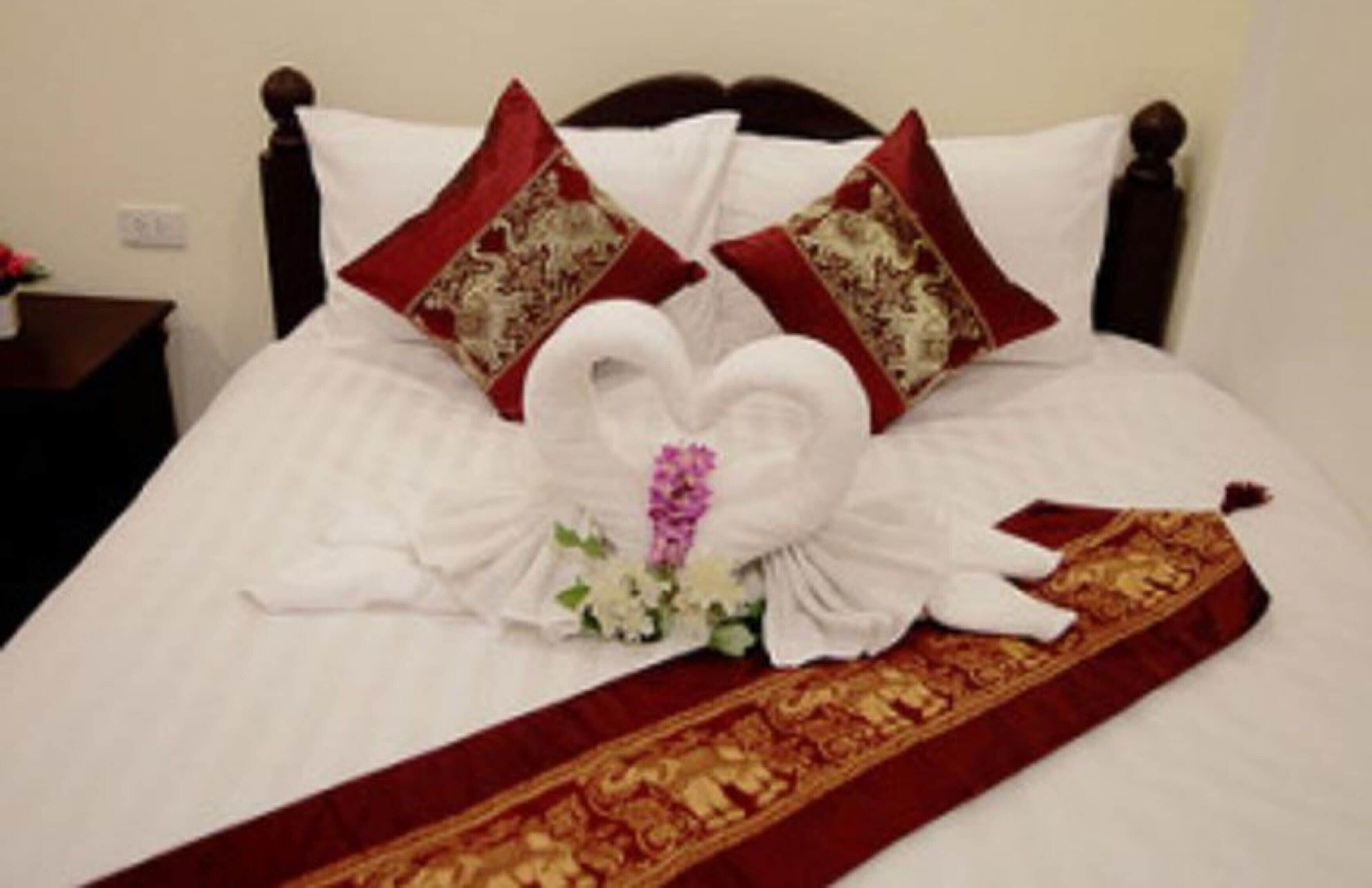 A neatly made bed with a heart-shaped towel arrangement and two decorative pillows.