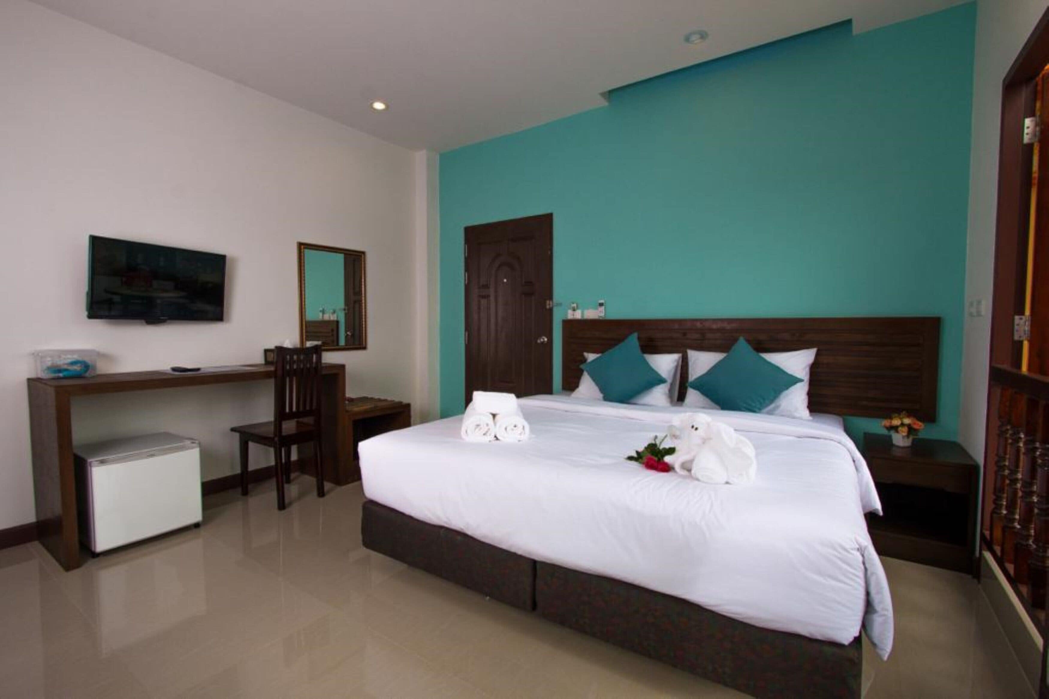 Habitación de hotel con cama, escritorio, silla, refrigerador pequeño y puerta.