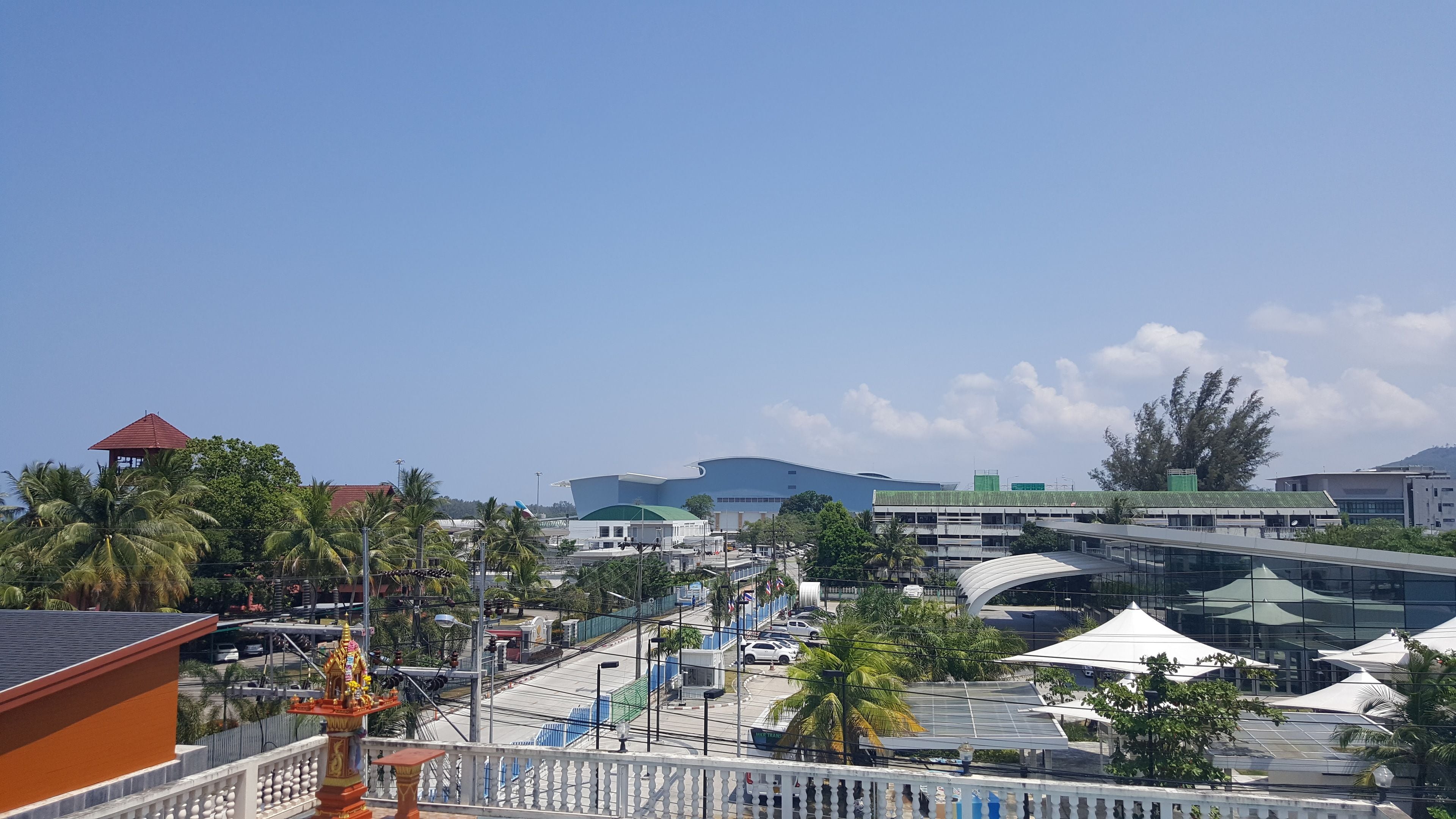 A modern building with a curved roof, surrounded by palm trees and a clear sky.
