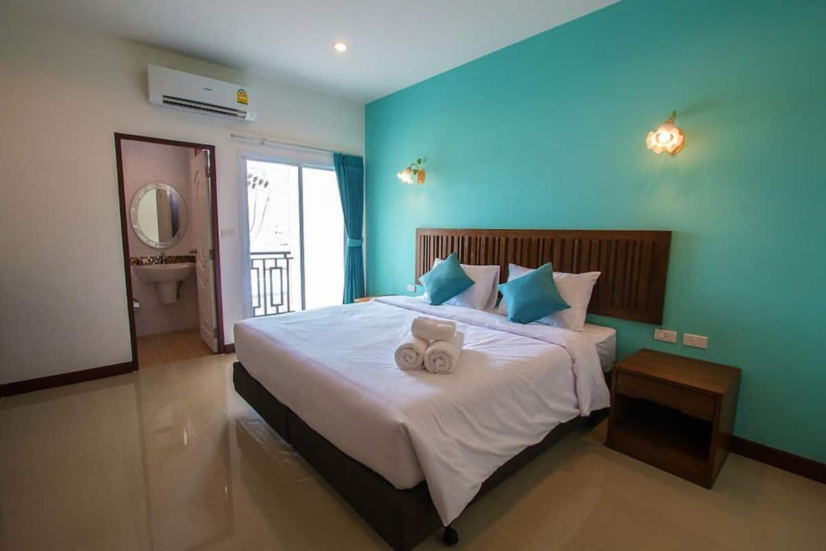 Une chambre d’hôtel avec un grand lit, une tête de lit en bois, une table de chevet, une salle de bain avec un miroir et un lavabo, et des murs de couleur turquoise.