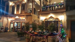 Un restaurante con terraza, plantas en macetas y luces colgantes.