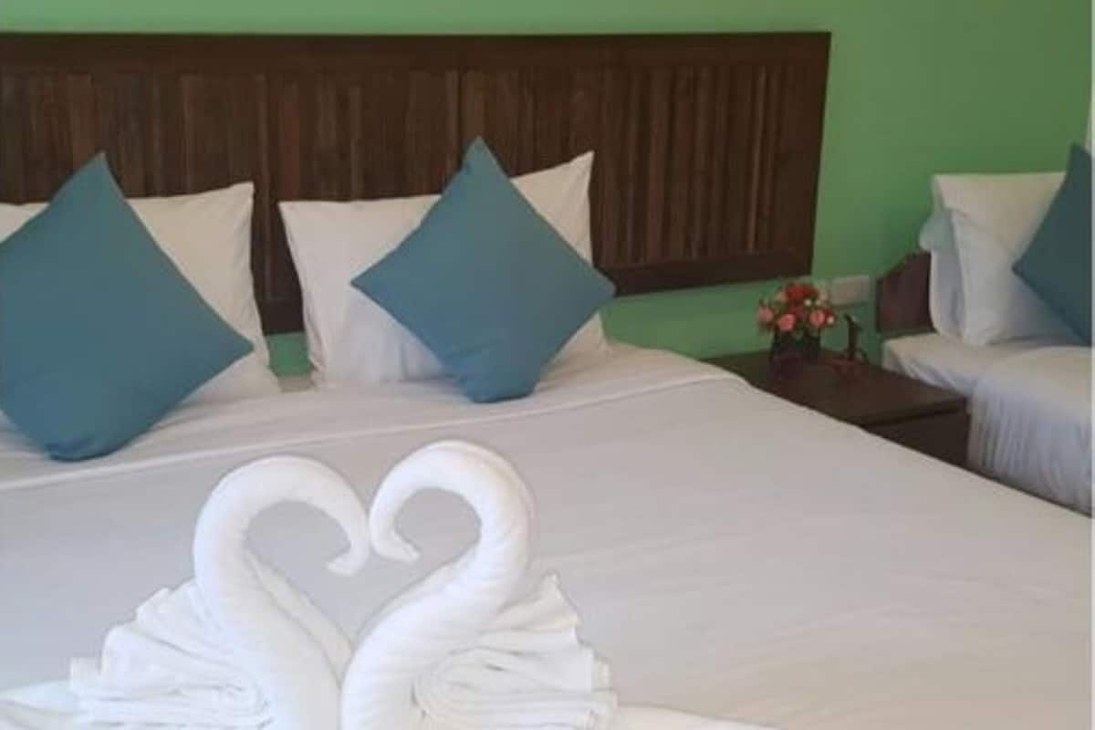 Une chambre d’hôtel avec un grand lit, deux oreillers, une tête de lit en bois et une table de chevet ornée d’un vase de fleurs.