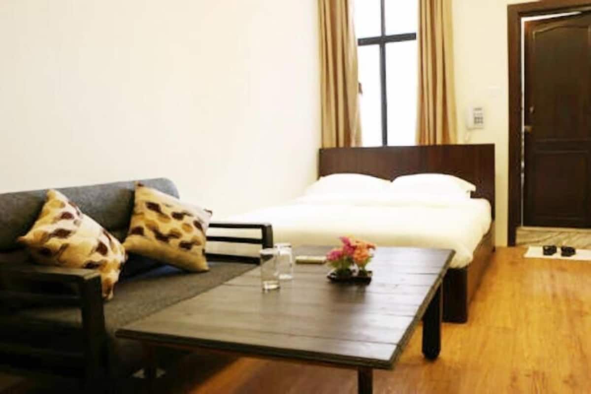 A room with a bed, a sofa, a table with a vase, and a window with curtains.