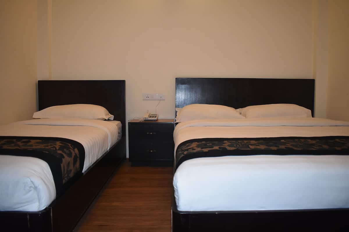 A hotel room with two single beds, each with a black headboard and white bedding. There is a small bedside table with a lamp and a power outlet between the beds.