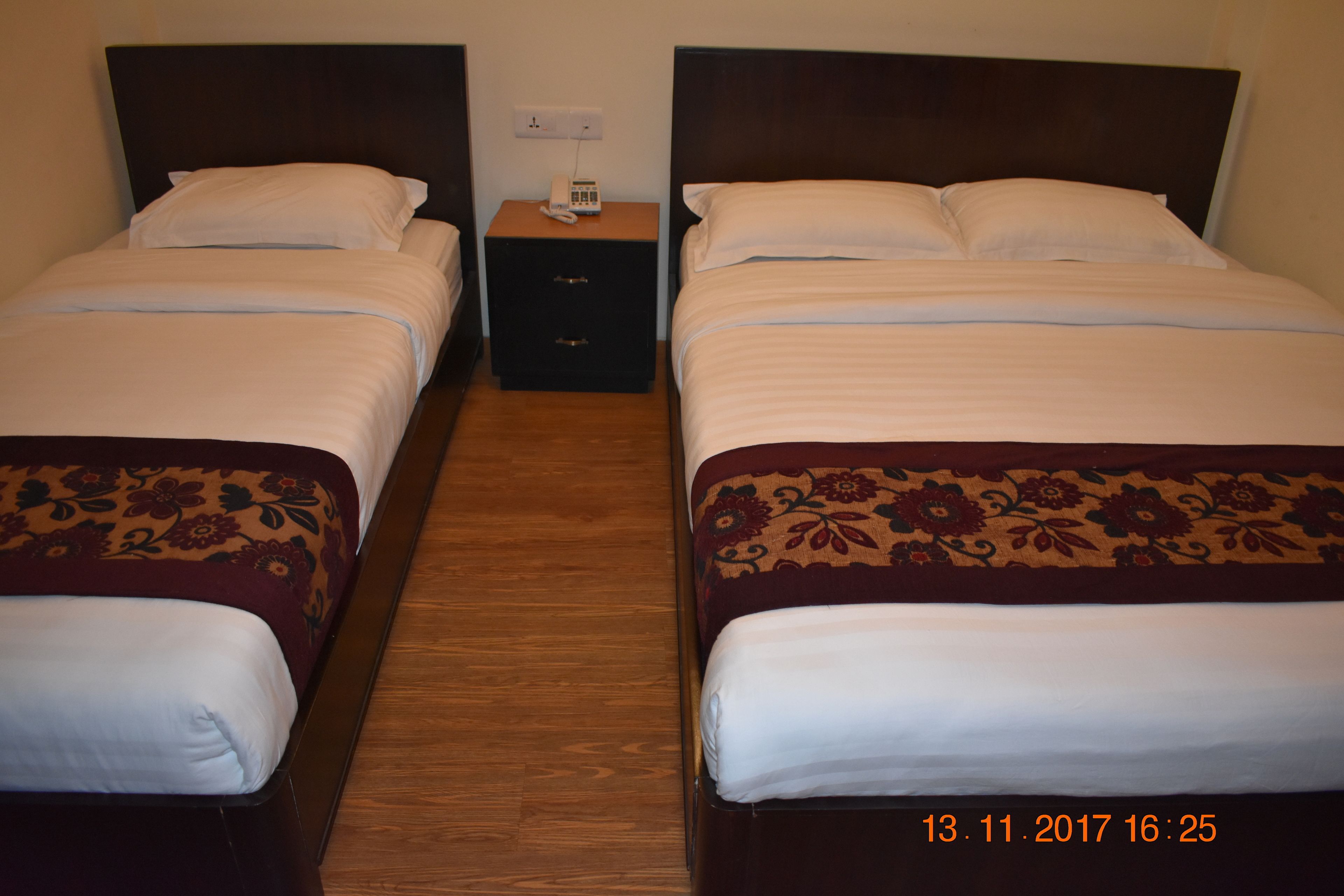 Quarto de hotel com duas camas de solteiro, cada uma com cabeceira de madeira, mesa de cabeceira com telefone e pequena gaveta.