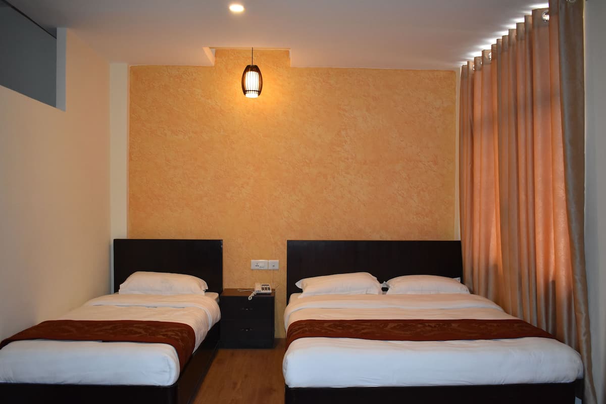 A hotel room with two beds, a nightstand, a wall-mounted light, and a window with curtains.