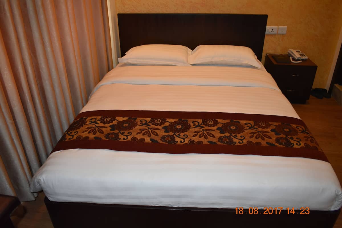 A neatly made bed with a floral-patterned bedspread, a bedside table with a phone, and a curtain partially drawn to the side.
