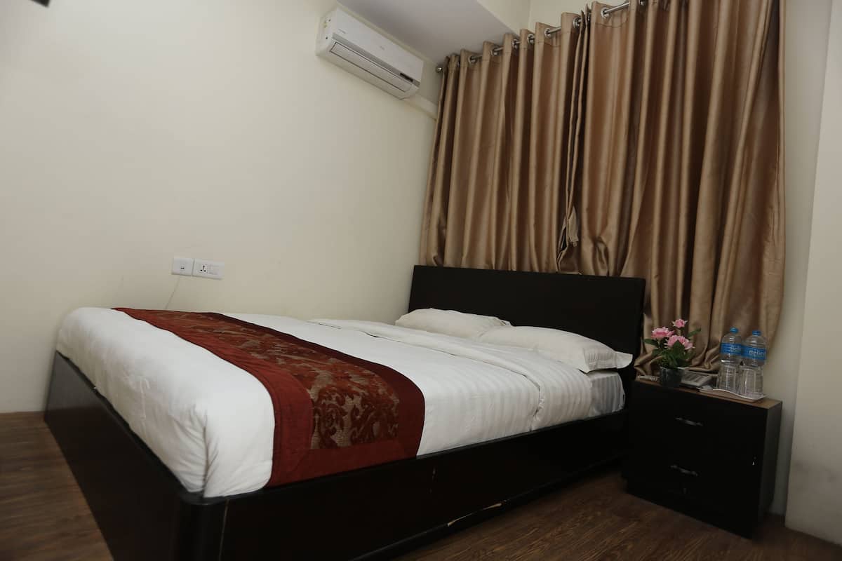 A bedroom with a bed, a nightstand, a wall-mounted air conditioner, and a window with curtains.