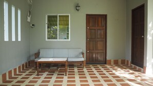 A room with a checkered floor, a wooden door, a bench, and a window with a view of greenery.
