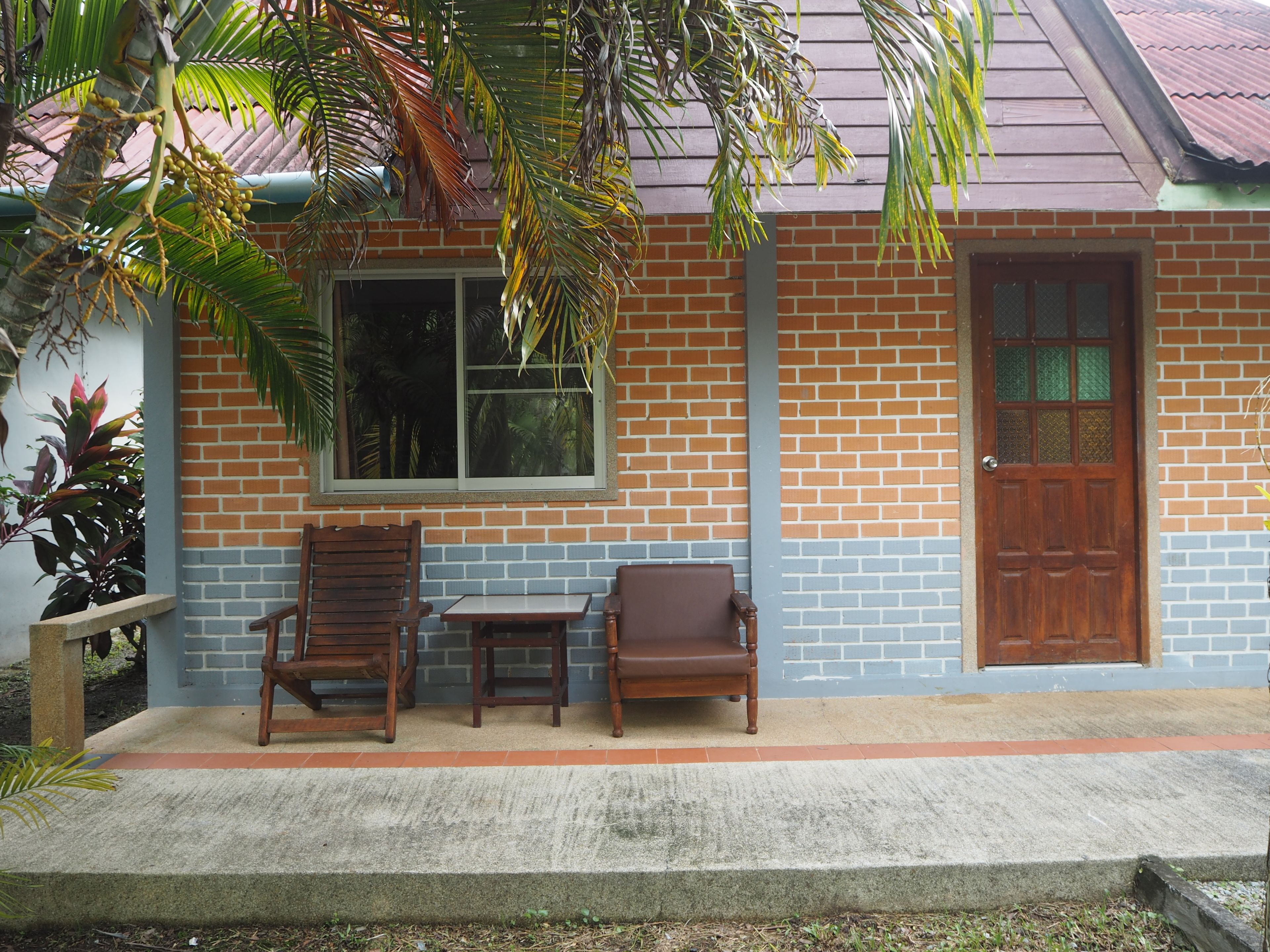 A building with a brick facade, a wooden door, and two wooden chairs outside.