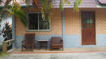 A building with a brick facade, a wooden door, and two wooden chairs outside.
